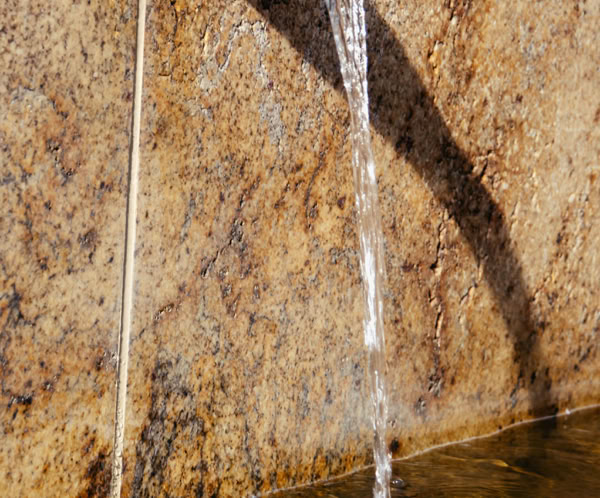 An elegant stream of water flows from a rustic stone wall into a peaceful pond below.
